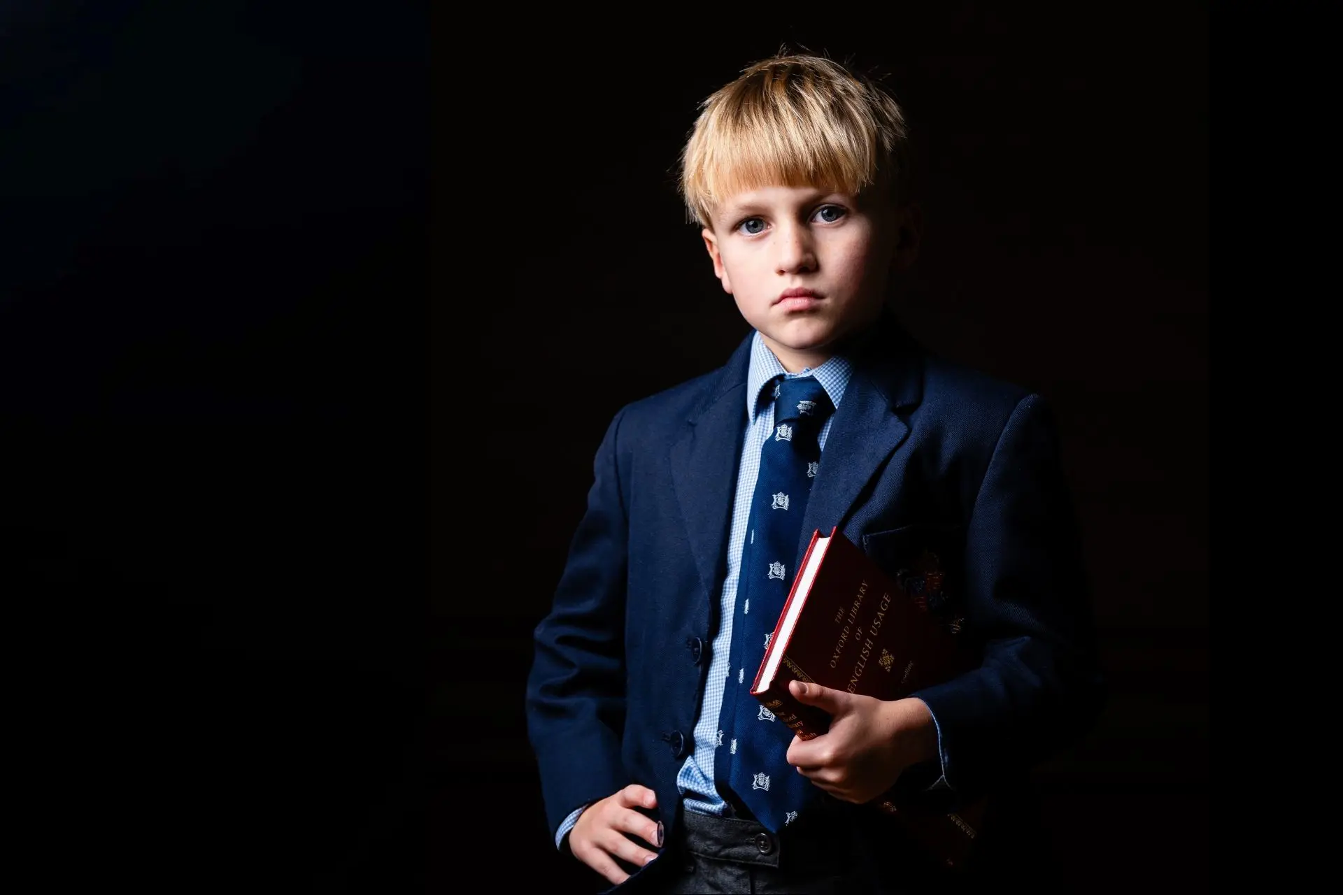 A prep boy in smart uniform, confidently holding an academic book.