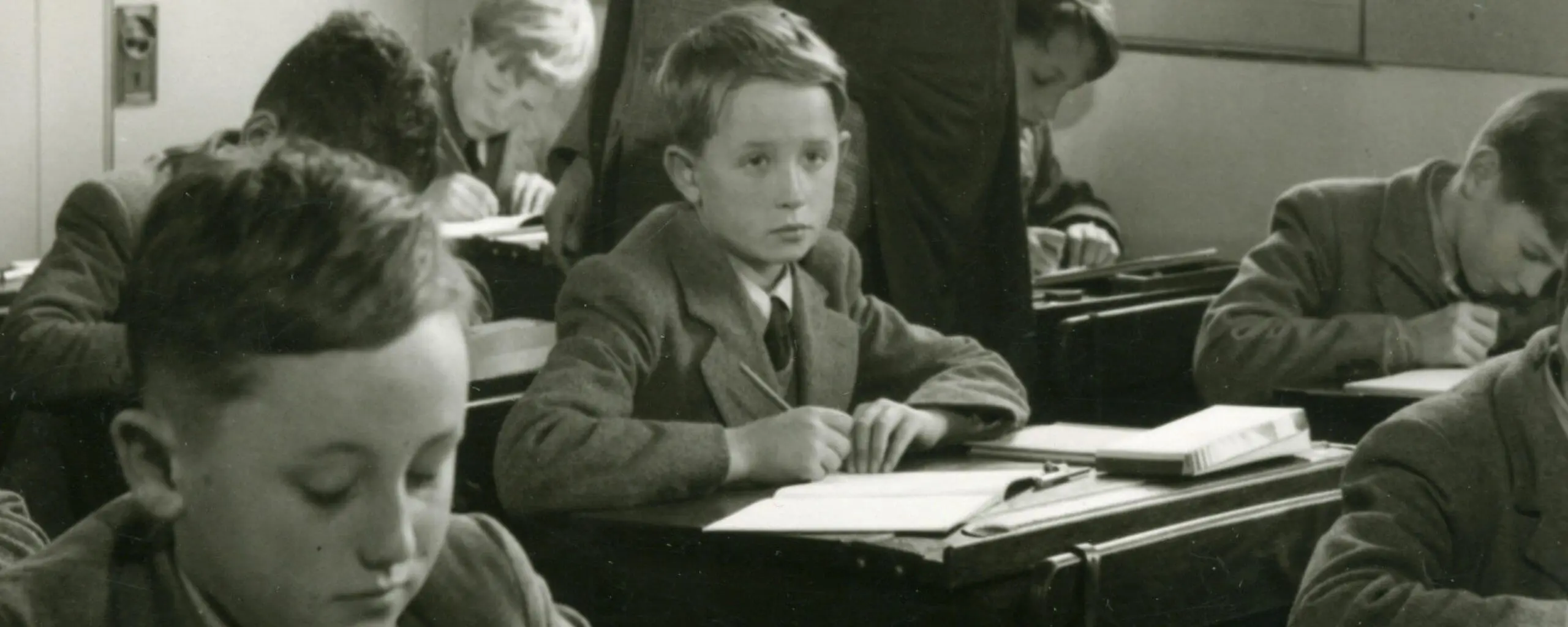 A vintage-style image of boys sitting solemnly in class.