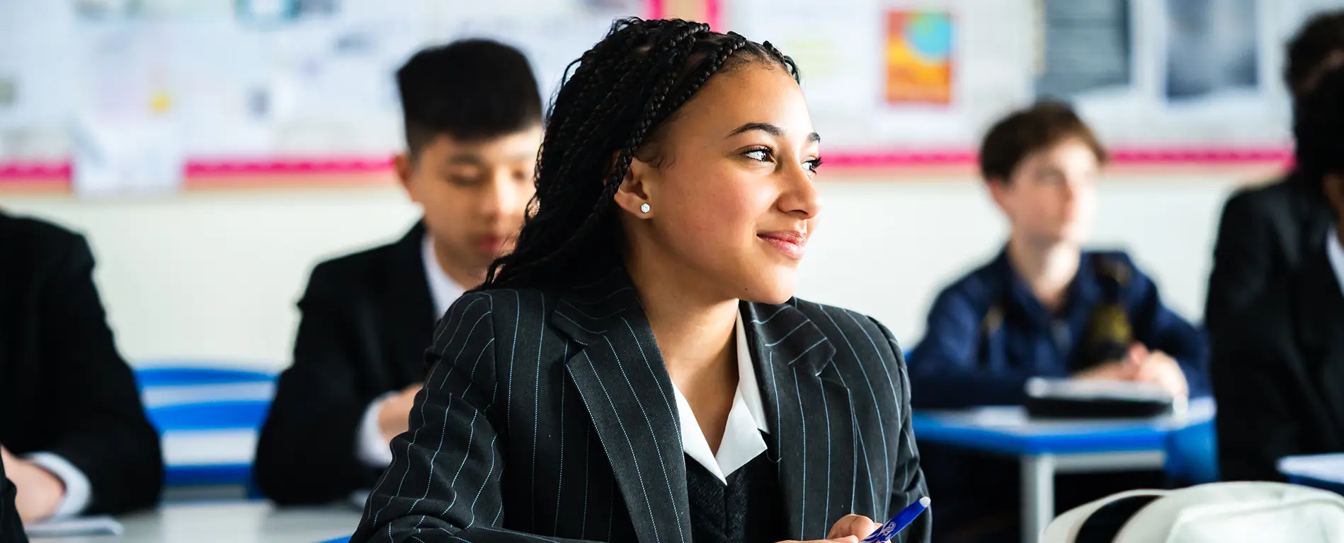 A senior girl in uniform, smiling as she looks out the classroom window.